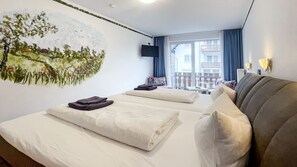 Et hotelværelse med to senge, et billede på væggen, et fjernsyn og en balkon med udsigt til bygninger.