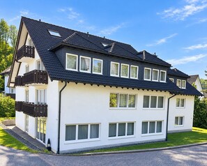 A two-story residential building with a dark roof, white exterior walls, and multiple windows. - Comfortable and versatile room -perfect for relaxation, work and exchange (Winterberg)