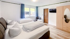 A bedroom with two beds, a chair, a TV, and a wardrobe. - A comfortable and versatile room—perfect for relaxation, work, and socializing (Winterberg)