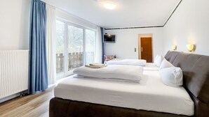A hotel room with a large window, a bed with white linens, a brown headboard, and a television on the wall. - Comfortable and versatile room -perfect for relaxation, work and exchange (Winterberg)