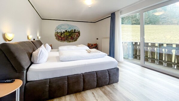 A modern bedroom with a large bed, a sofa, a small table, and a painting on the wall.