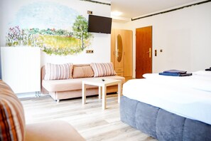 A bedroom with a bed, a sofa, a TV mounted on the wall, and a wardrobe. - Comfortable and versatile room -perfect for relaxation, work and exchange (Winterberg)