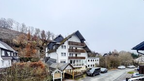 A multi-story building with balconies, a covered entrance, and a parking area with cars. - Comfortable and versatile room -perfect for relaxation, work and exchange (Winterberg)