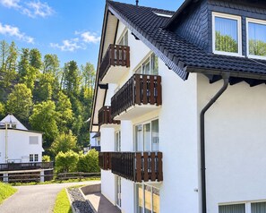 A multi-story building with balconies, a pathway, and a forested background. - Comfortable and versatile room -perfect for relaxation, work and exchange (Winterberg)