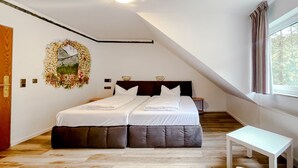 A bedroom with a large bed, a bedside table, a small table, and a window with curtains. - Comfortable and versatile room -perfect for relaxation, work and exchange (Winterberg)