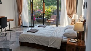 A hotel room with a bed, a desk, and a chair. There is a view of a garden through the window. - Villa Kiprey (Karangasem)