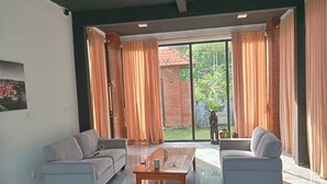 A modern living room with two grey sofas, a wooden coffee table, and large windows with orange curtains. - Villa Kiprey (Karangasem)
