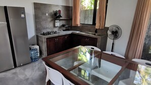 A modern kitchen with a built-in gas stove, a large water dispenser, and a glass-top dining table. - Villa Kiprey (Karangasem)