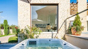 Une maison moderne dotée d’une grande fenêtre, d’un jacuzzi et d’un patio agrémenté de plantes.
