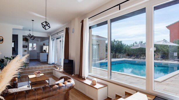 Un salon moderne avec un canapé en cuir, un coin repas et une grande fenêtre donnant sur une piscine.