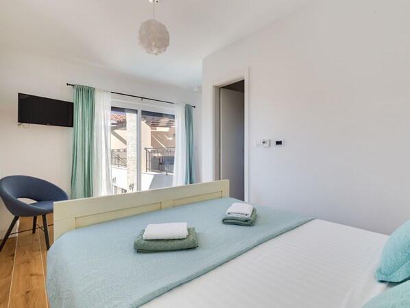 Une chambre avec un lit, une chaise, une télévision et un balcon donnant sur une vue agréable.