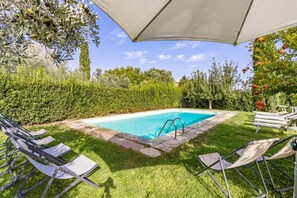 Una piscina con agua cristalina azul, rodeada por un césped cuidado y varias árboles.