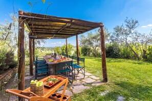 Un espace de restauration en plein air agrémenté d’une pergola en bois rustique, d’un sol en pierre et offrant une vue sur un paysage verdoyant et luxuriant.