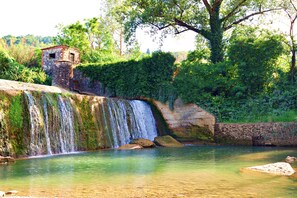Ein Wasserfall stürzt in ein klares Becken, in der Nähe befindet sich eine Steinstruktur.