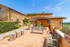 Un patio con un banco de madera, plantas en macetas y un muro de piedra.
