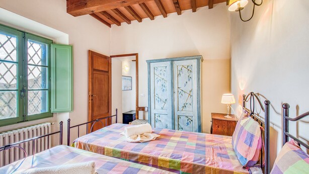 Ein Schlafzimmer mit karierter Bettdecke, einer Holztür und einem Fenster mit grünen Rollläden.