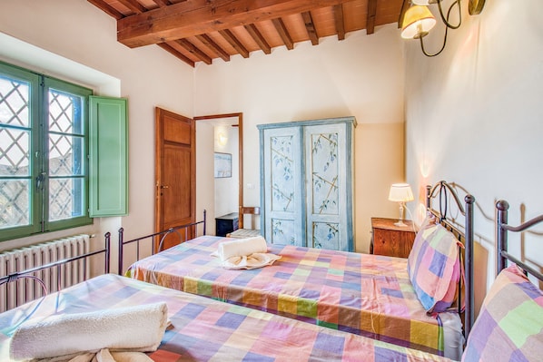 A bedroom with a checkered bedspread, a wooden door, and a window with green shutters. - Villa Salivolpe Chianti Views & Private Pool for 18, San Casciano VDP, Italy (San Casciano VDP)