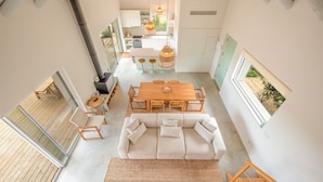 Un intérieur moderne avec une table à manger en bois, un canapé blanc et un coin cuisine équipé d’une cuisinière et de luminaires suspendus.