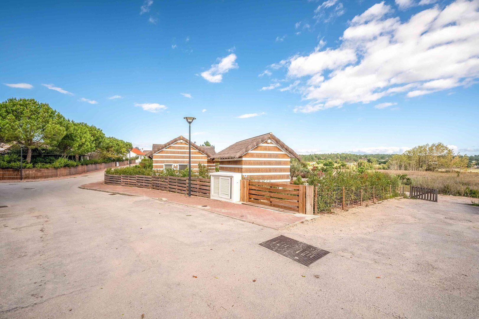 A rural setting with a wooden cabin and a small building, surrounded by greenery and a clear sky.