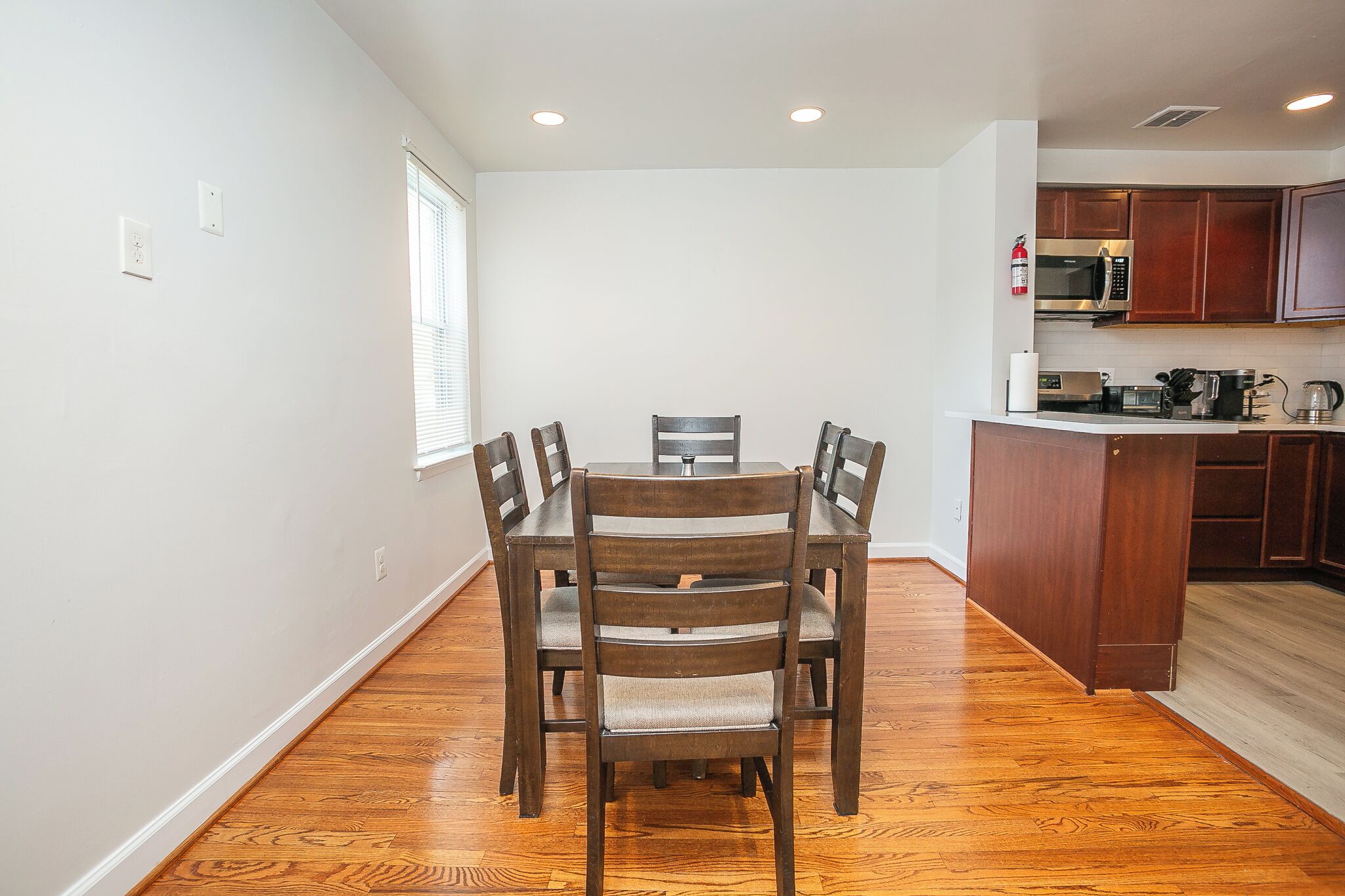 Un comedor con mesa y sillas de madera, una cocina con armarios de madera y una ventana con persianas.