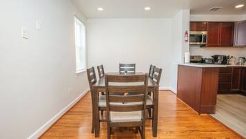 A dining area with a wooden table and chairs, a kitchen with wooden cabinets, and a window with blinds.