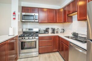 A modern kitchen with stainless steel appliances, wooden cabinets, and a white countertop.