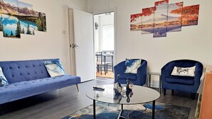 A modern living room with a blue sofa, a glass coffee table, and two blue armchairs. - 2 Bedroom House in Leeds - Sleeps 5, WiFi, Pets (Leeds)