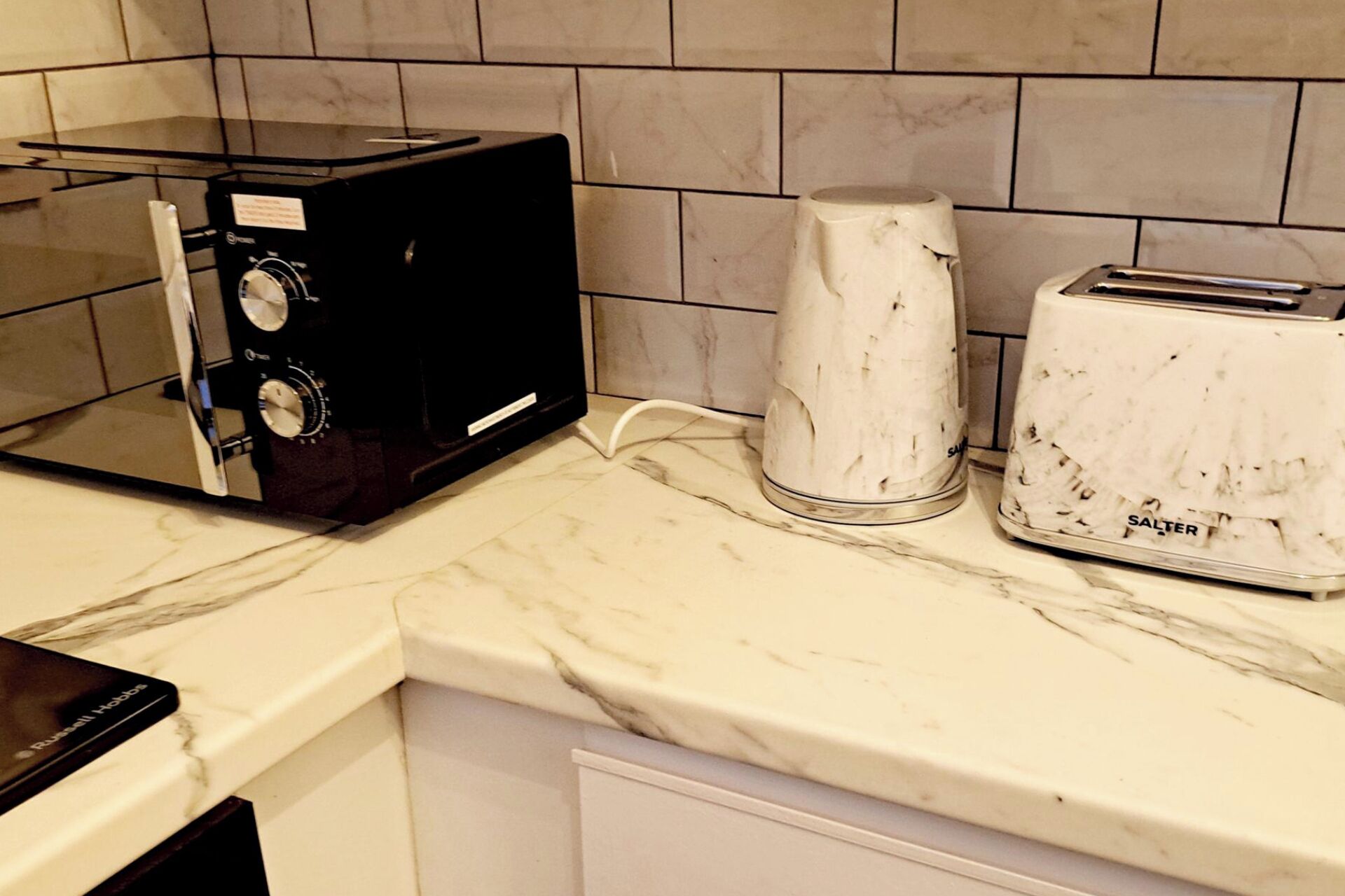 A kitchen with a black microwave, a white electric kettle, and a white toaster.