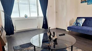 A modern living room with a glass coffee table, a blue sofa, and a radiator. - 2 Bedroom House in Leeds - Sleeps 5, WiFi, Pets (Leeds)