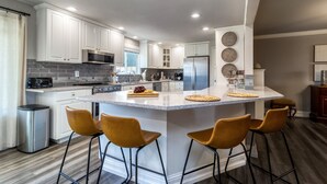 Une cuisine moderne avec des armoires blanches, un grand îlot central doté de tabourets, des appareils en acier inoxydable et un design épuré et contemporain.