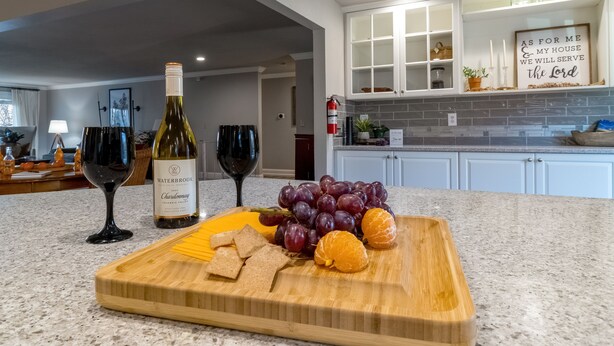 Une cuisine dotée d’un plan de travail en marbre, d’une planche à découper avec des raisins, des oranges et du fromage, et d’une bouteille de vin.