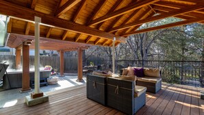 Une terrasse extérieure couverte, dotée d’un plancher en bois, de meubles en osier et d’une structure en forme de pergola.