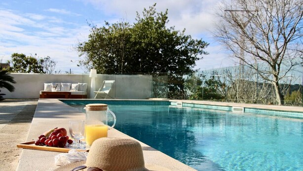 A poolside setting with a table featuring a pitcher of orange juice, grapes, and a straw hat.