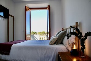 A bedroom with a bed, pillows, a bedside table with a lamp, and a view of the outdoors through an open door. - Mater Randa,  history peace and Solidarity (Randa)