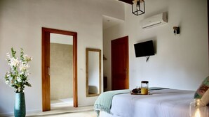 A bedroom with a bed, bedside table, lamp, mirror, and a vase with flowers.