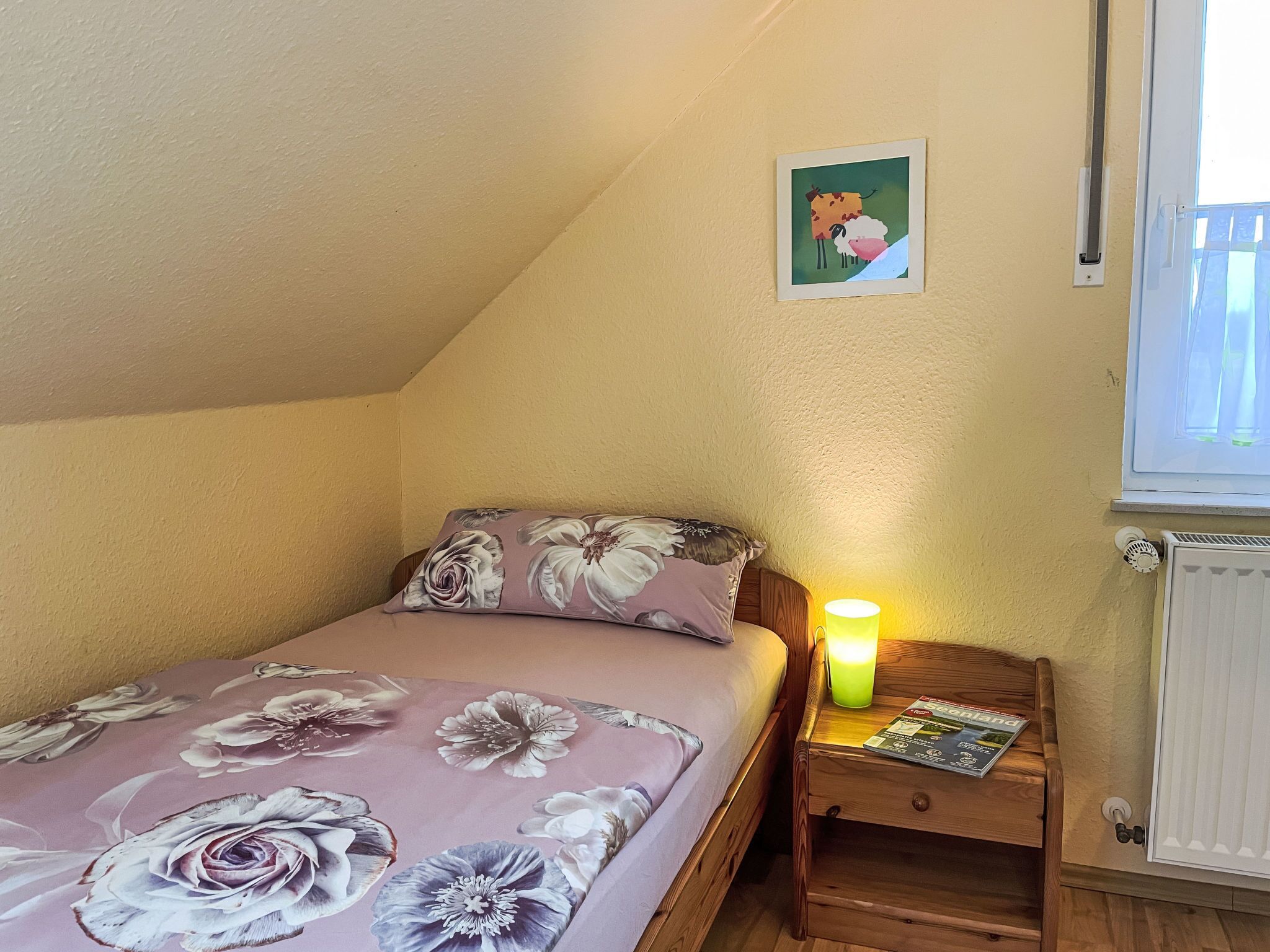 Un dormitorio con una cama individual, una mesita de noche con lámpara, un cuadro en la pared y una ventana con persianas.