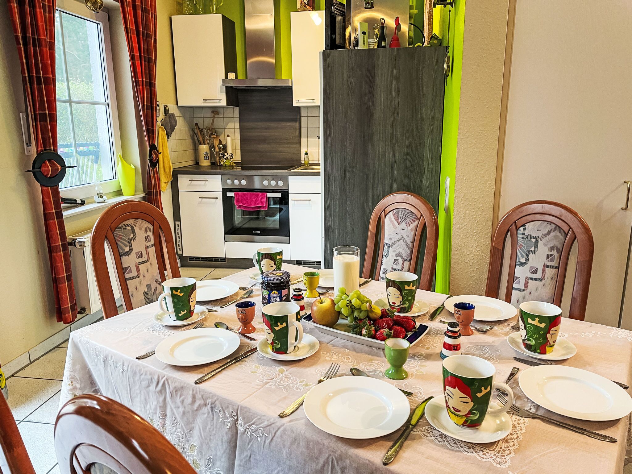 A dining table set with plates, cutlery, and festive mugs, with a kitchen in the background.