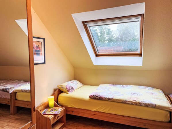 A bedroom with a sloped ceiling, a skylight, a wooden bed frame, a nightstand with a lamp, and a framed picture on the wall.
