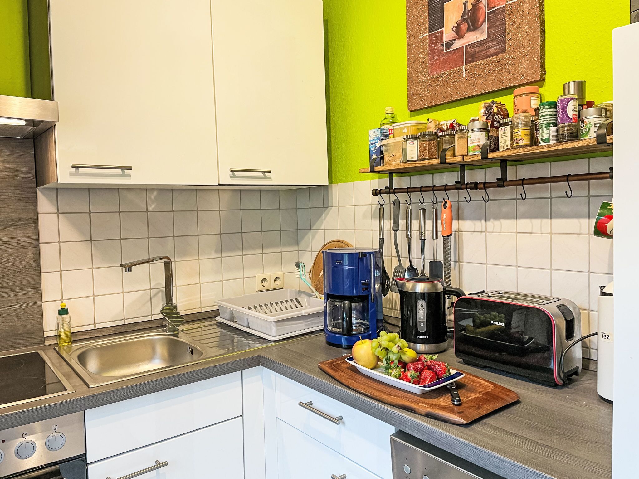 Een moderne keuken met witte kasten, een roestvrijstalen spoelbak, een koffiezetapparaat, een broodrooster en een fruitschaal op het aanrecht.