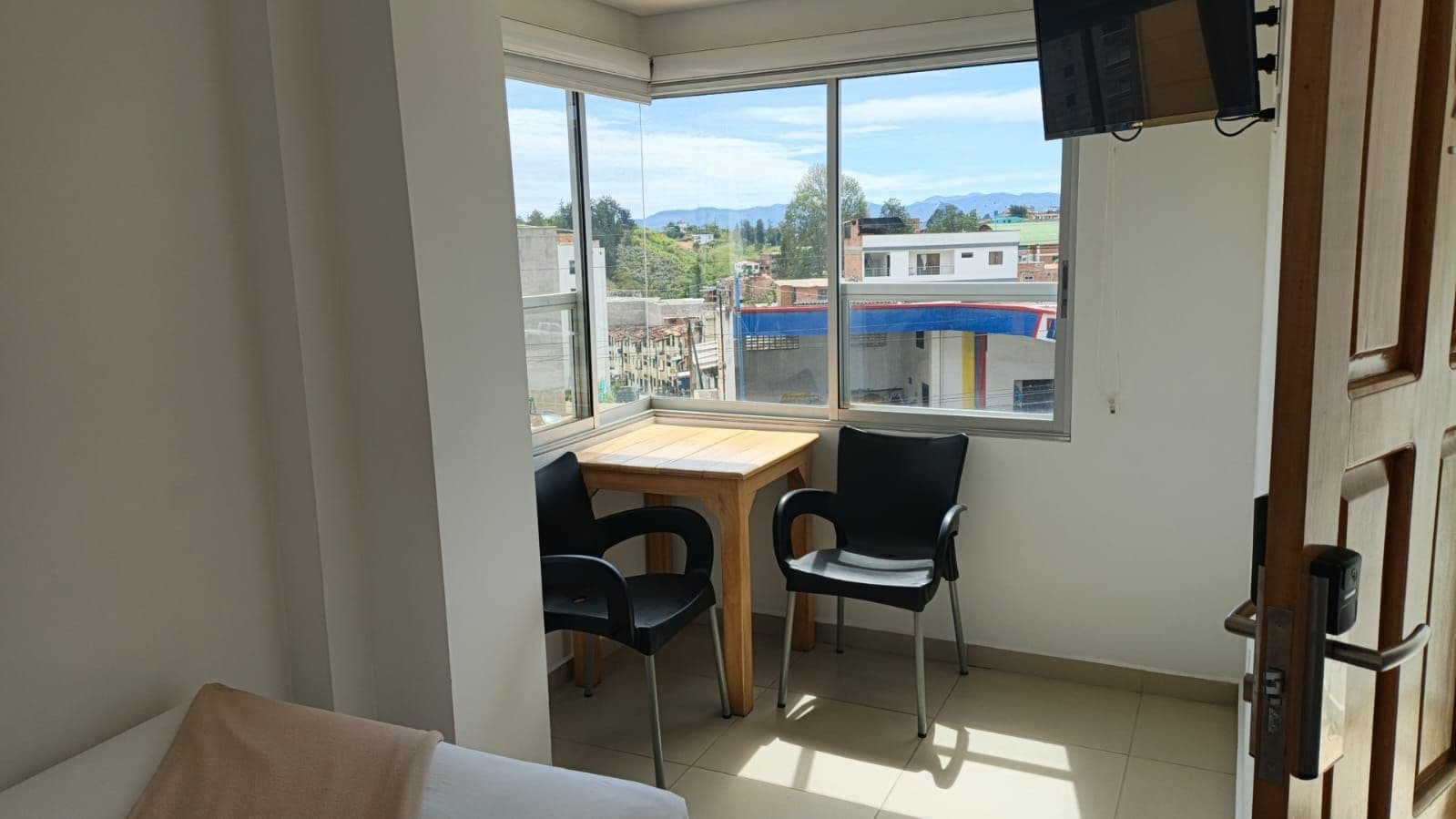 Una habitación con ventana, una mesa, dos sillas y una puerta.