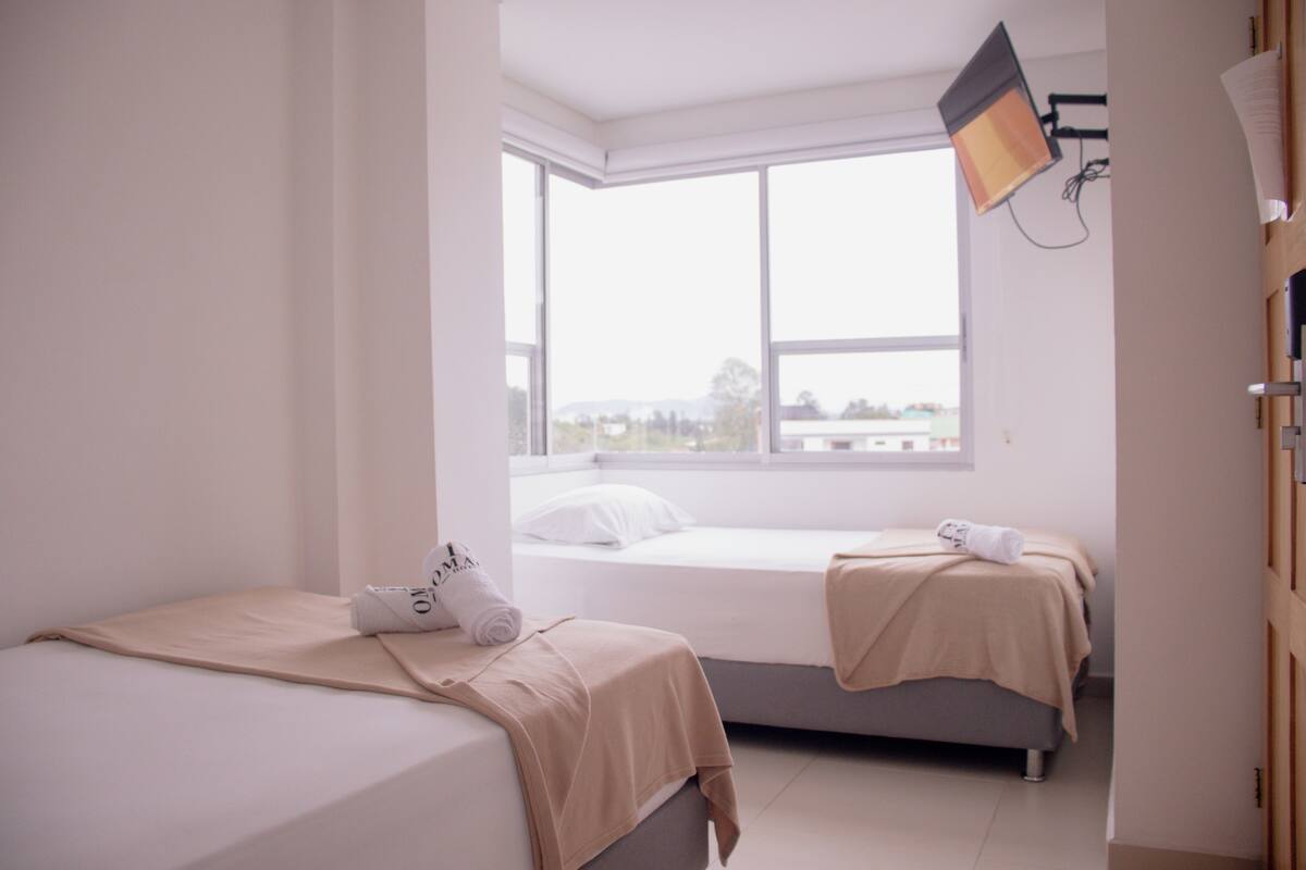 Un dormitorio con dos camas, un ventanal grande y una lámpara fijada al techo.