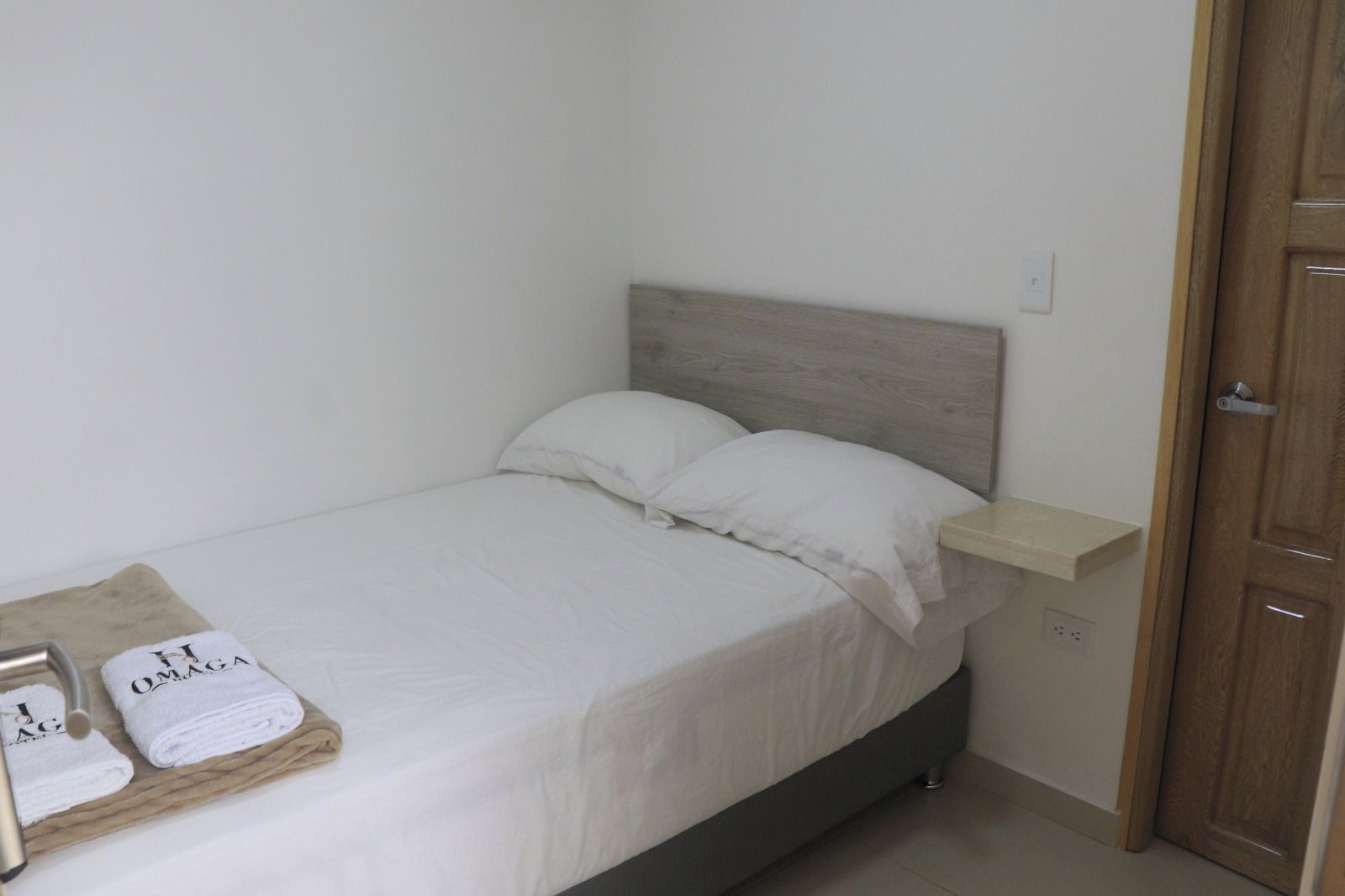 A single bed with a wooden headboard, a bedside table, and a towel on the floor.