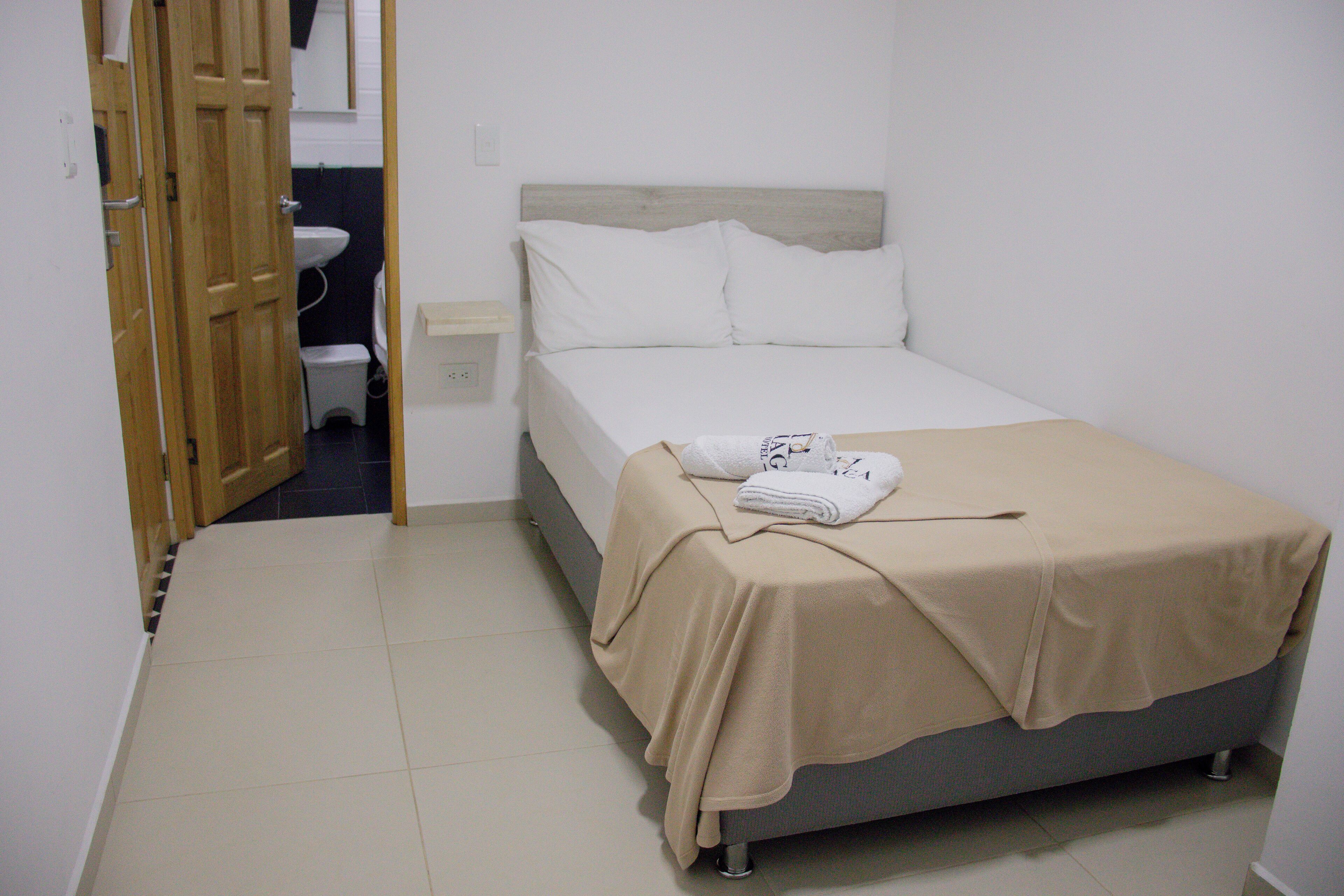 A bedroom with a bed, a bedside table, a nightstand, a wooden door, a white sink, and a mirror.