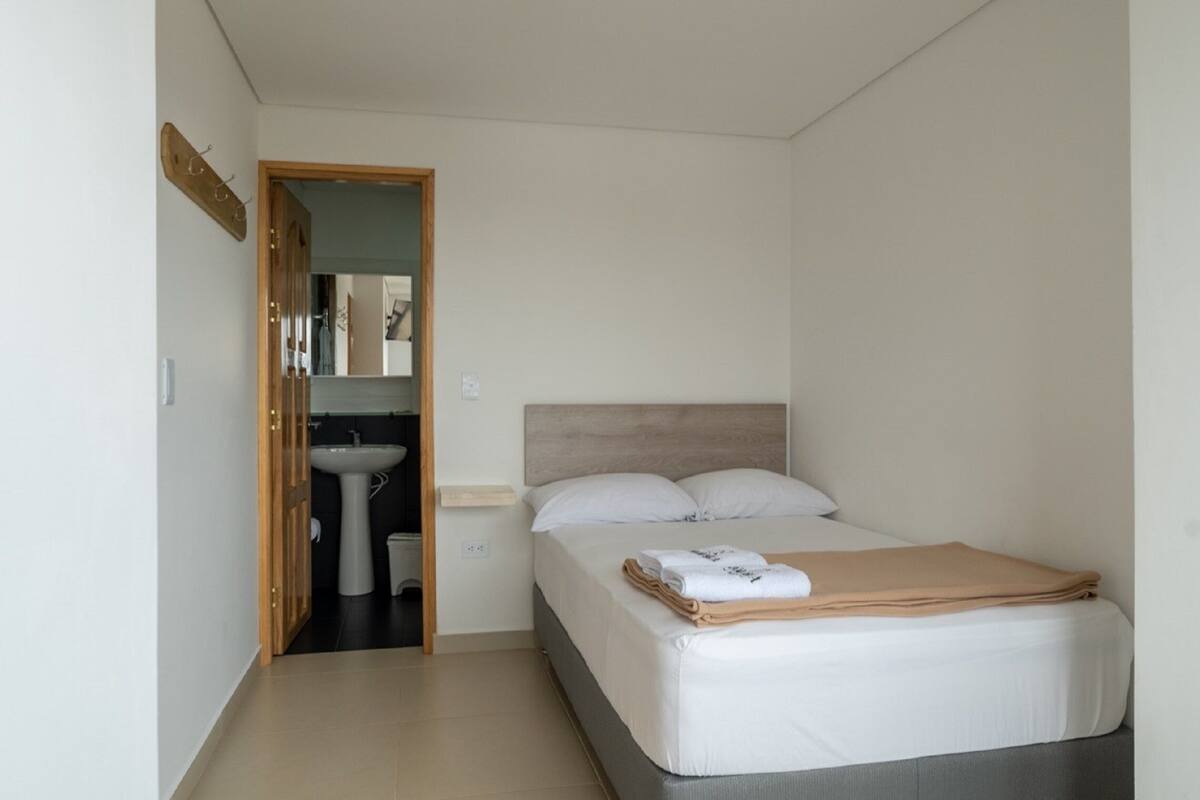 Un dormitorio con cama, mesita de noche, espejo y puerta que da a un baño.
