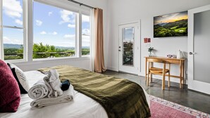 A hotel room with a bed, a desk, a TV, and a view of the outdoors. - Fall Mtn Views | Hot Tub · Game Room · 10m AVL (Asheville)
