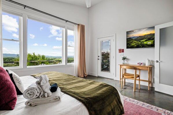 Une chambre d’hôtel équipée d’un lit, d’un bureau, d’une télévision et offrant une vue sur l’extérieur.