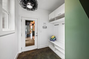 Een gang met een witte deur, een spiegel, een plank met tassen en een groene muur.