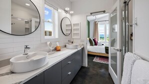 A modern bathroom with a large mirror, two sinks, and a shower. - Fall Mtn Views | Hot Tub · Game Room · 10m AVL (Asheville)