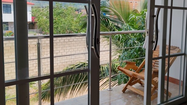 A room with large sliding glass doors leading to a balcony with a view of greenery and buildings.
