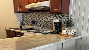 A kitchen with wooden cabinets, a tiled backsplash, a marble countertop, a coffee maker, and two white bar stools.